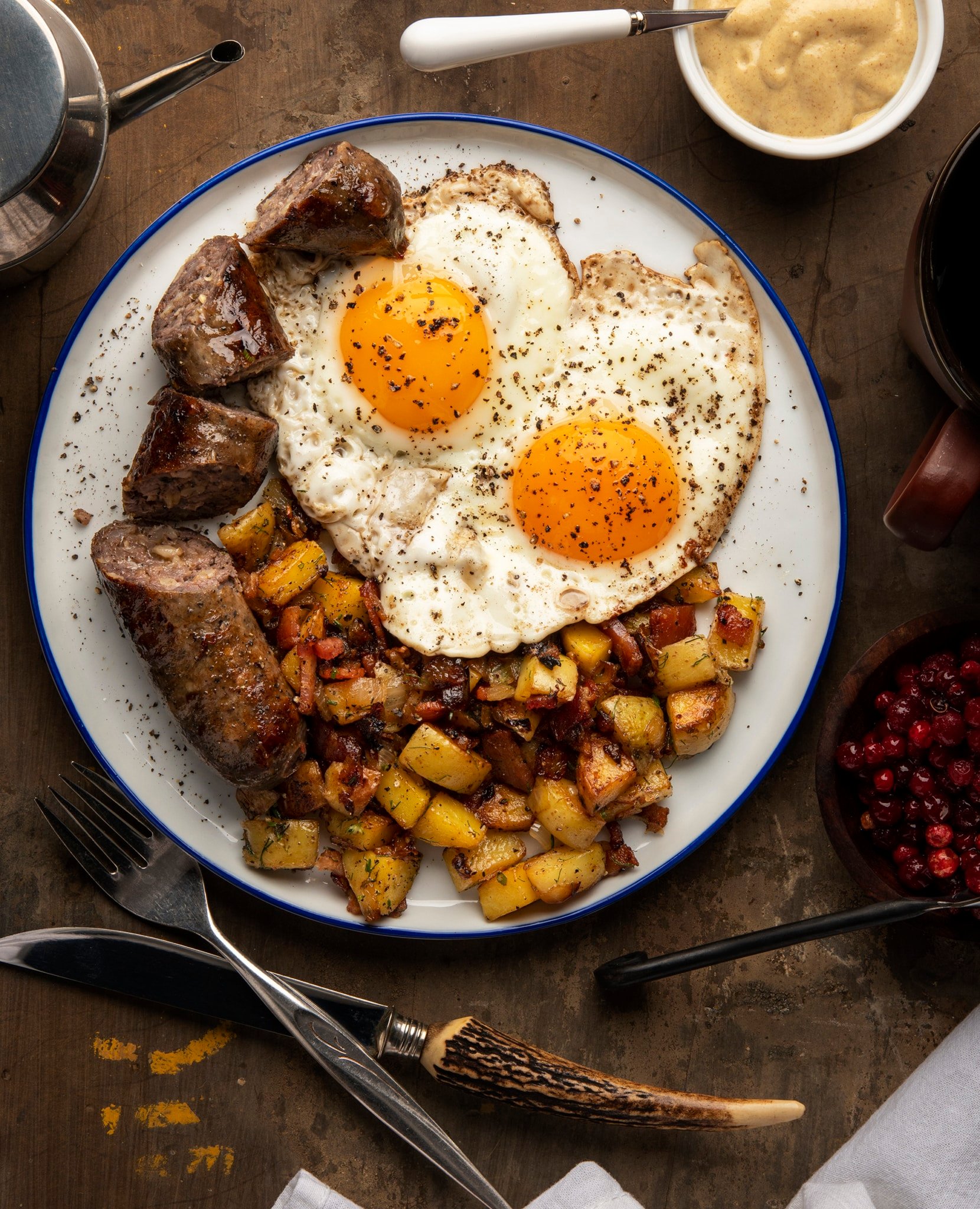 A plate with Swedish sausage, fried potatoes and sunny side up eggs. 