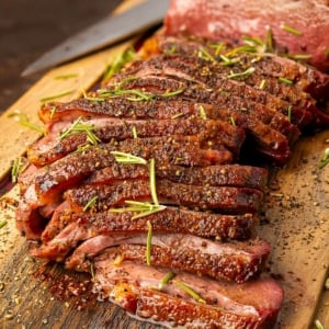 A simple goose breast recipe of thinly sliced Canada goose breast with rosemary and black pepper on a cutting board.