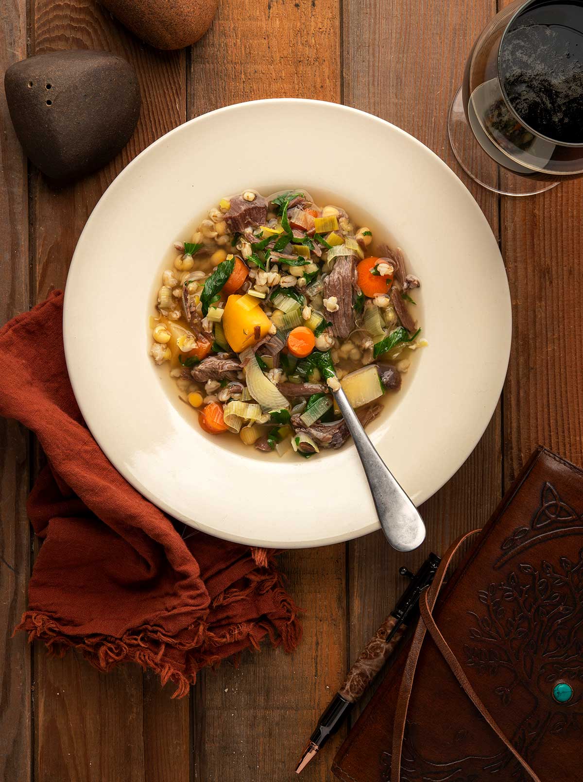 A bowl of Scotch broth, venison soup. on a table with a glass of beer. 
