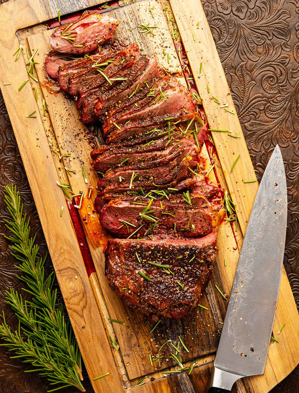 A sliced Canada goose breast on a cutting board with black pepper and rosemary. 