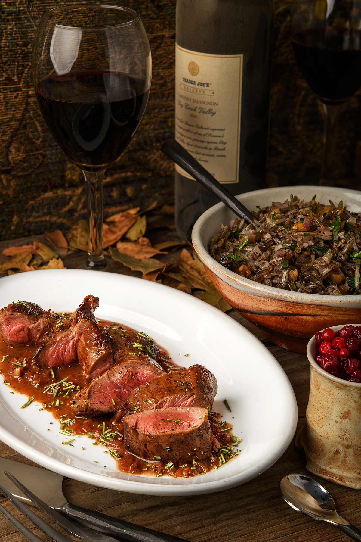 A platter of venison tenderloin with a pan sauce, with wild rice in the background. 