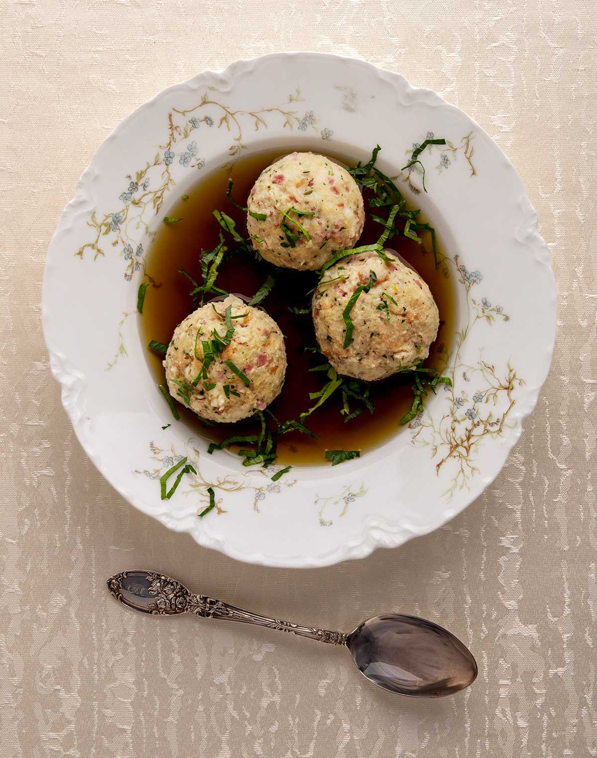 A bowl with three canederli dumplings in broth. 