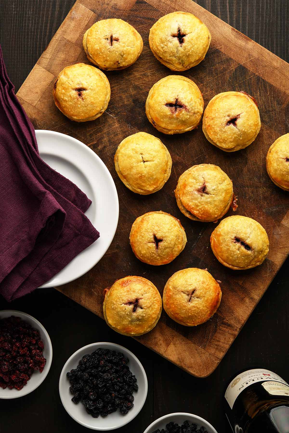 Lots of venison mincemeat pies on a cutting board with bowls of dried fruit. 