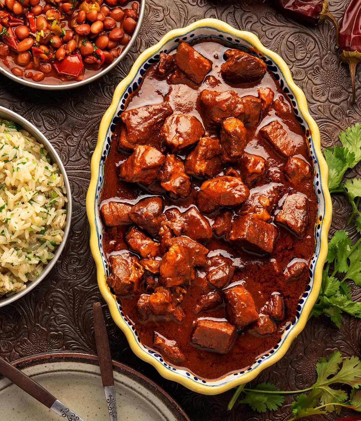 A bowl of asado de puerco with beans and rice alongside. 