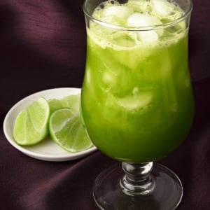 A glass of cucumber agua fresca with some limes alongside.