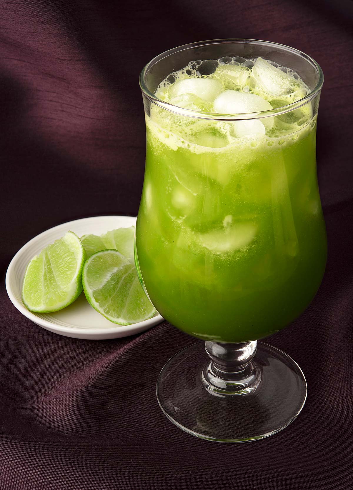 A glass of cucumber agua fresca with some limes alongside. 
