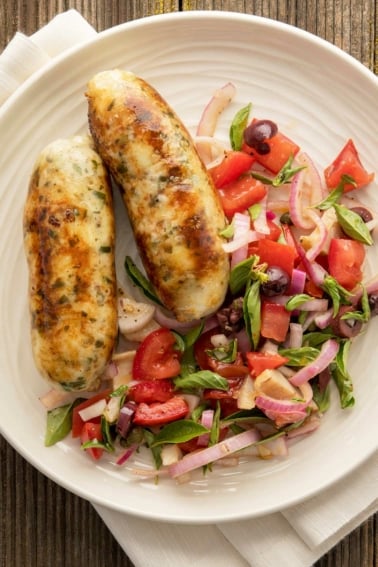 Grilled fish sausage on a plate with a summer salad.