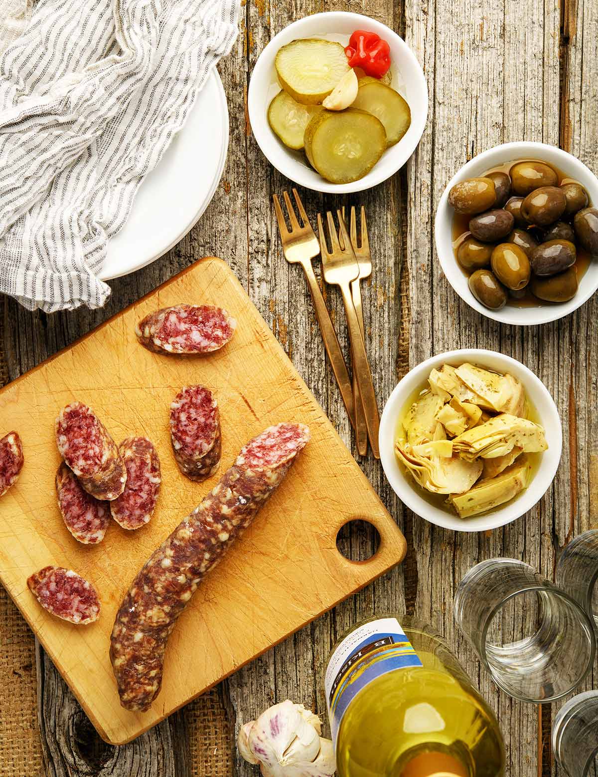 Spanish fuet sausage sliced on a cutting board with pickles alongside. 