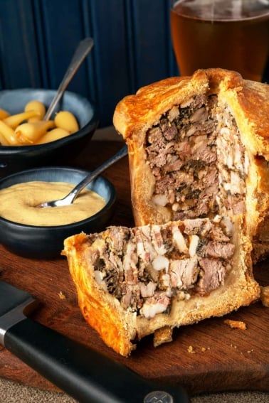 A British game pie with a wedge sliced out, showing the interior.