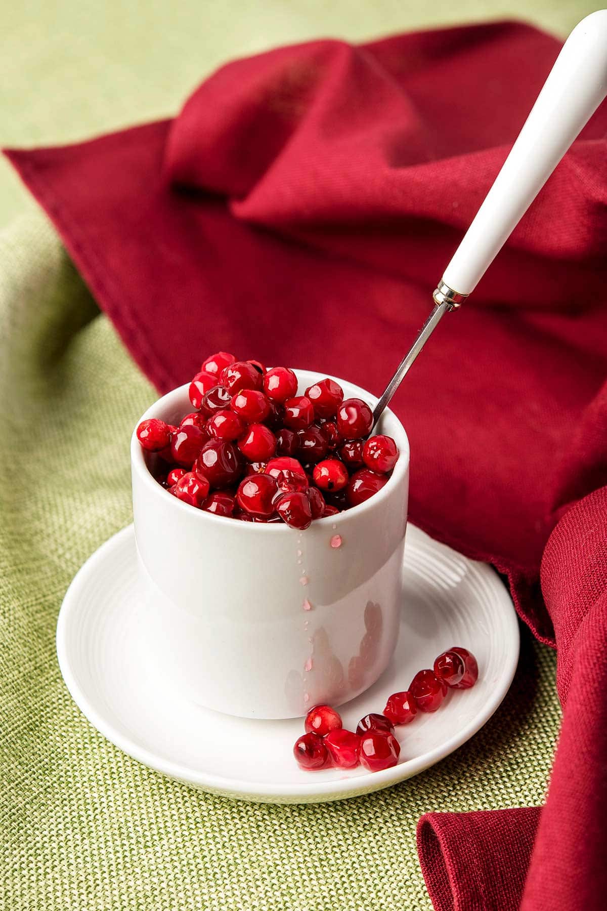 A small bowl of lingonberry sauce with a spoon in it. 
