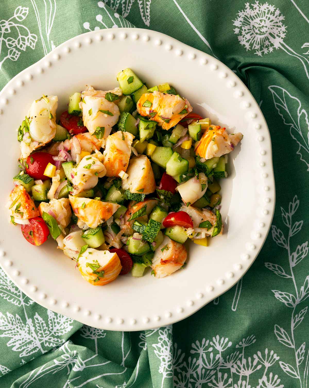 A plate of lobster salad with cucumbers, tomatoes, peppers and herbs. 