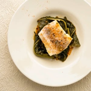A plate of sake poached fish with greens and togarashi.