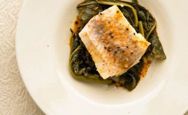 A plate of sake poached fish with greens and togarashi.