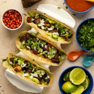 Three ribeye tacos in a taco holder with accompaniments.