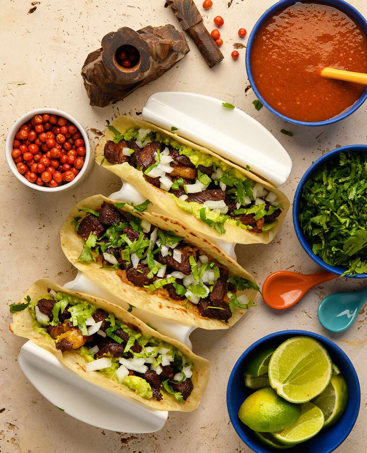 three ribeye tacos in a taco holder, with chiltepin chiles and other accompaniments. 