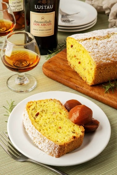 A slice of olive oil rosemary cake with some preserved fruit and sherry.