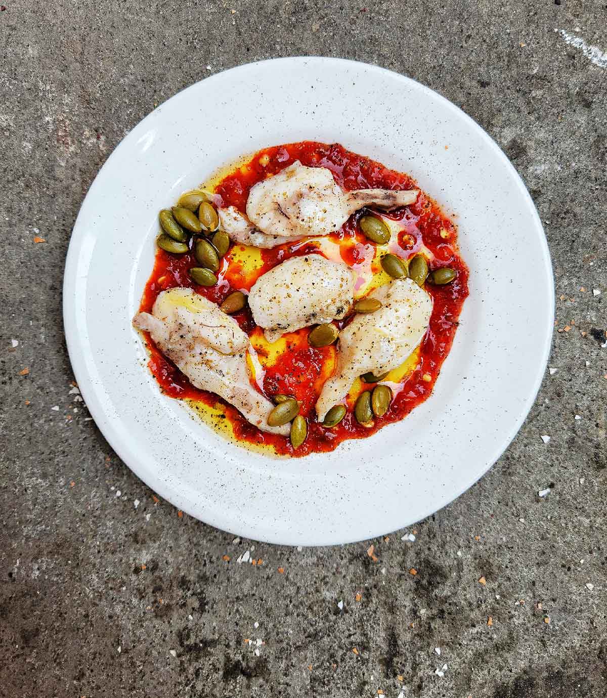 A plate of burbot cheeks with sambal, olive oil, roasted pumpkin seeds and pepper. 