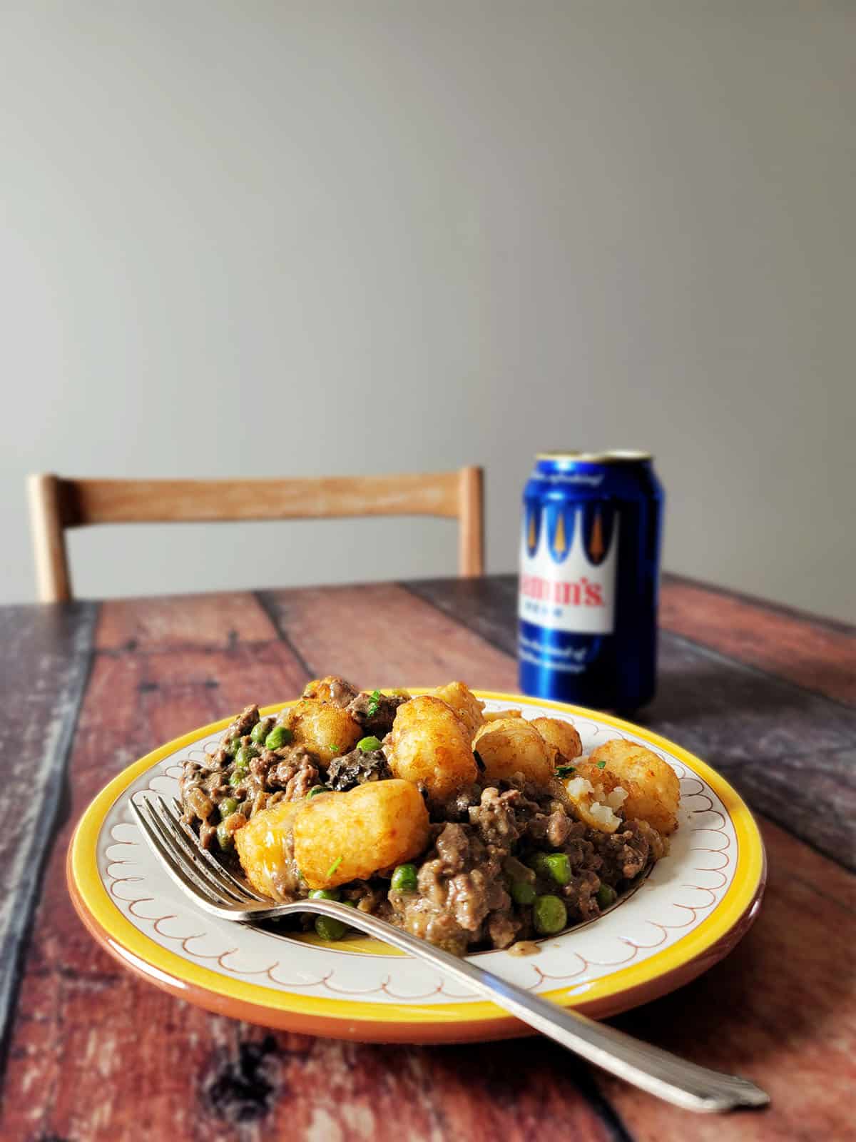 A serving of venison hotdish on a plate with a beer. 