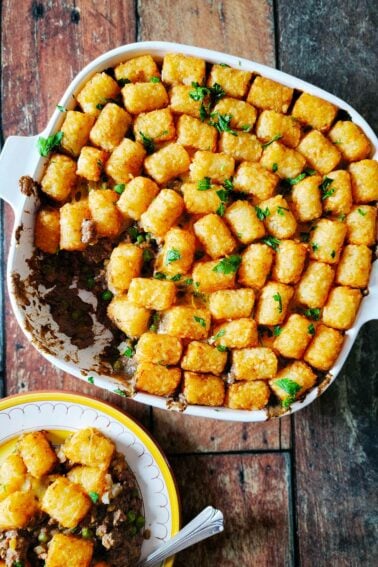 A casserole dish of tater tot hotdish with a plate of the meal alongside.