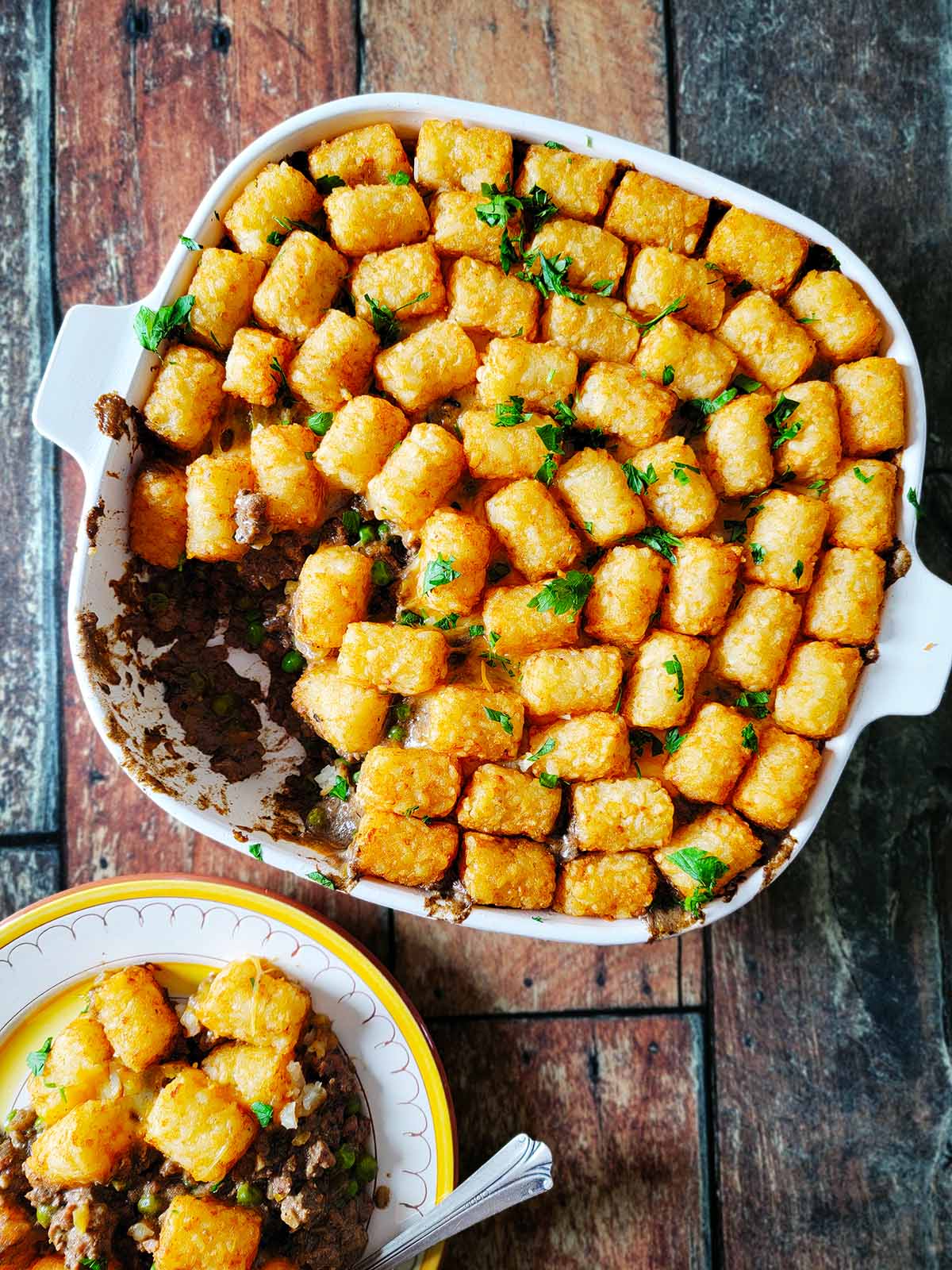 A casserole dish of tater tot hotdish with a plate of the meal alongside. 