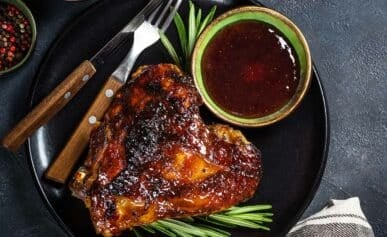 A barbecued turkey thigh on a plate with sauce.