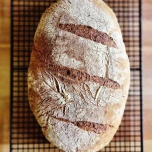 A loaf of rye sourdough cooling on a rack.