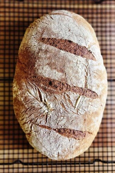 A loaf of rye sourdough cooling on a rack.