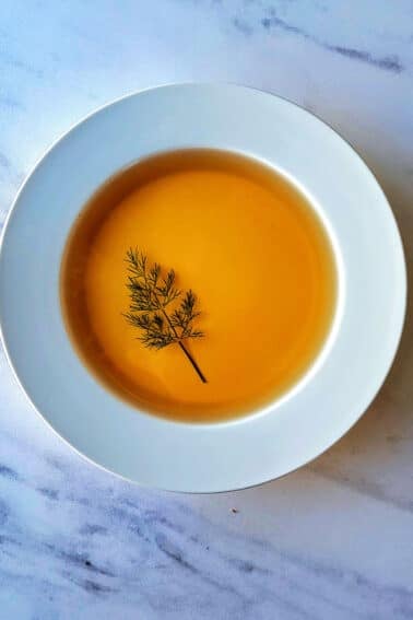 A bowl of chicken consomme with a dill leaf garnish.