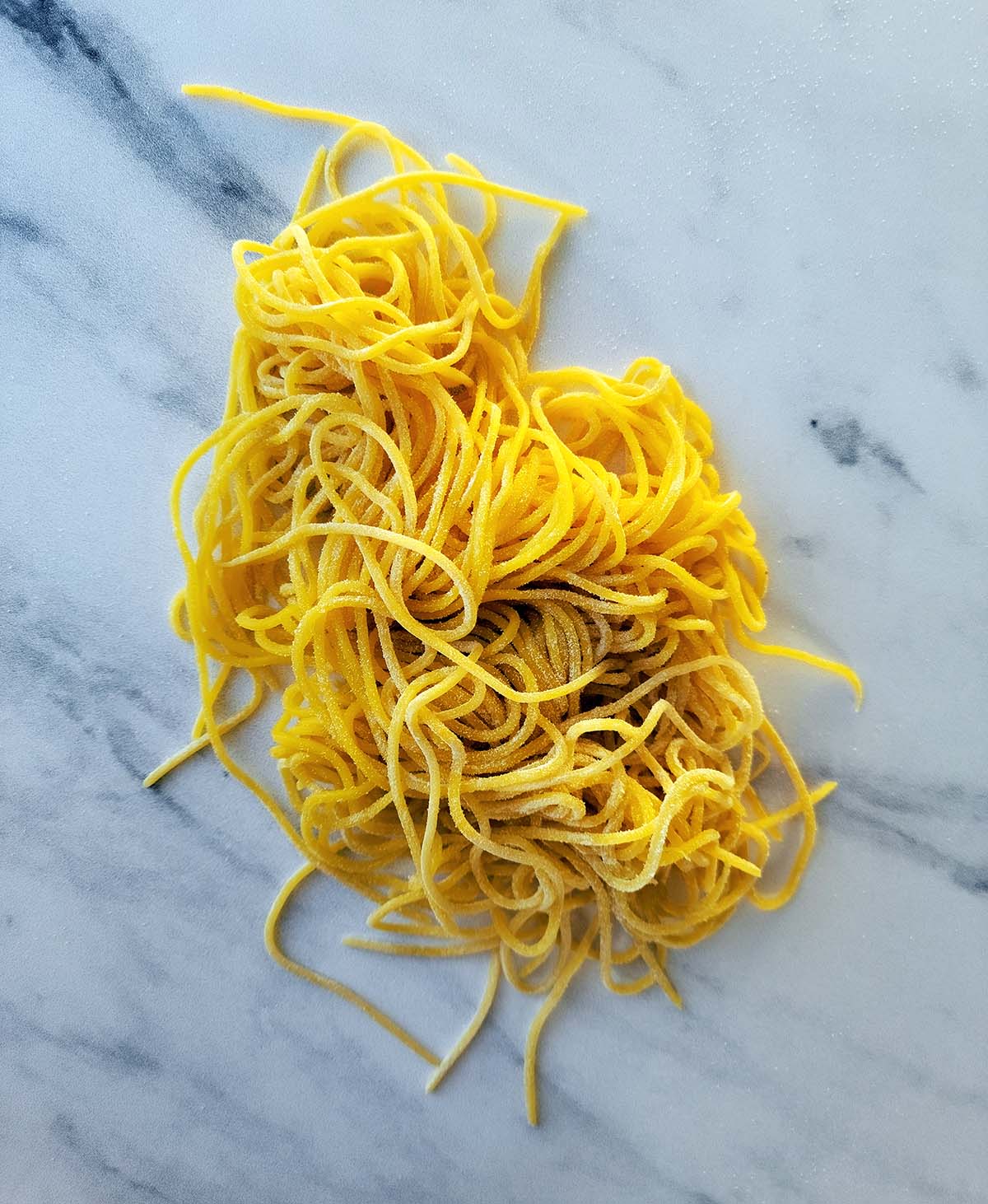 A nest of uncooked tajarin pasta on a marble board. 