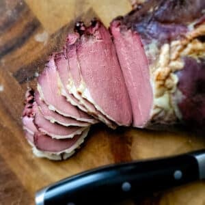 A tjalknol venison roast on a cutting board, sliced thin.