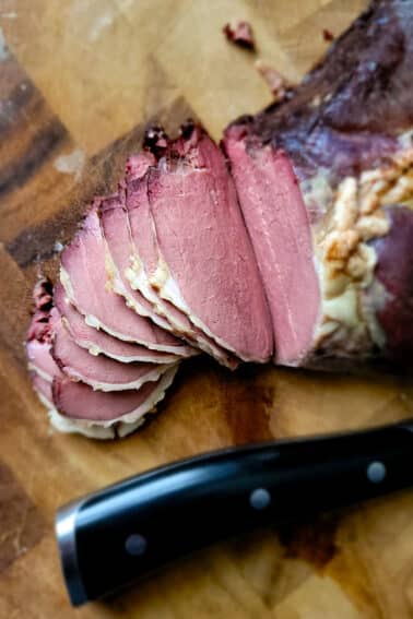 A tjalknol venison roast on a cutting board, sliced thin.