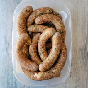 A plastic container of uncooked green onion sausages.