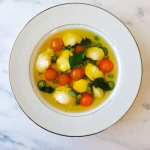 A bowl of clear fish soup with walleye cheeks and cherry tomatoes.