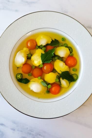 A bowl of clear fish soup with walleye cheeks and cherry tomatoes.